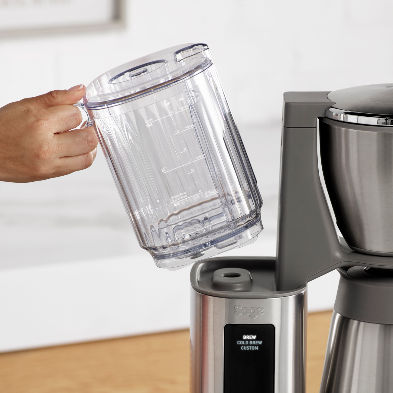 Person pouring from a clear container into a Sage Luxe Brewer™ Thermal Coffee Maker on a kitchen counter.