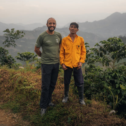 Two men standing in a mountainous landscape with greenery.